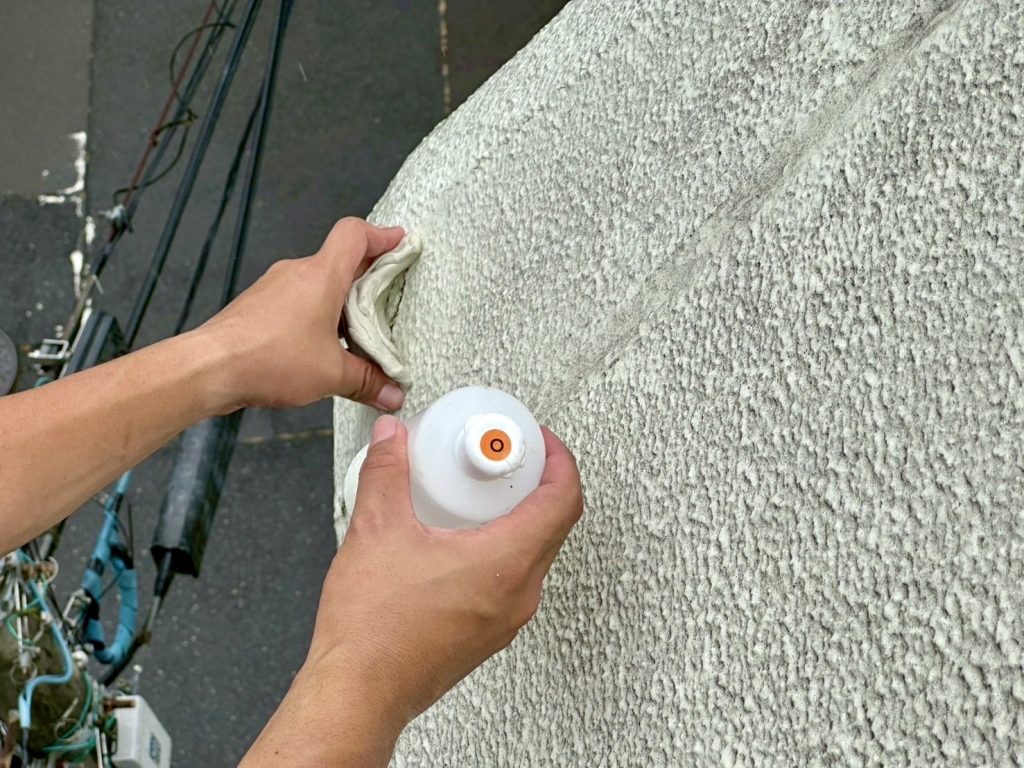 外壁の隙間に調査液を注入している様子。散水試験により雨水の浸入箇所を確認中。