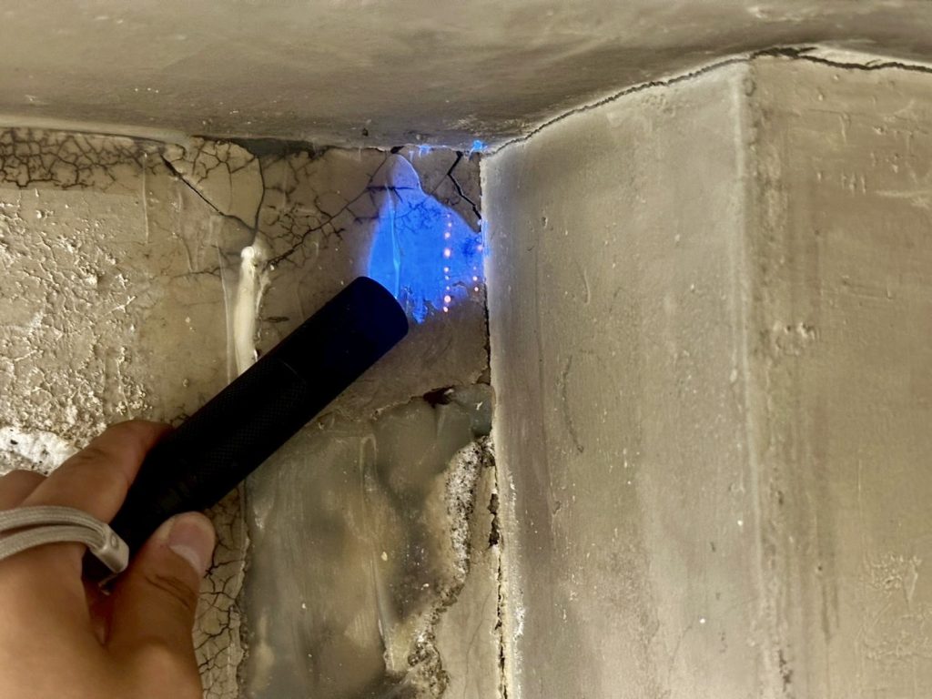 室内壁のクラック部分にブラックライトを当て、調査液の発光を確認している場面。