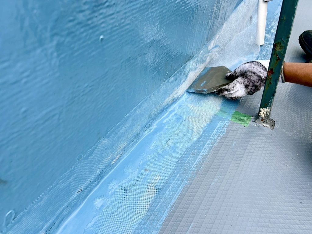 屋上の端部・立ち上がり部分へウレタン防水材を塗っている様子の写真